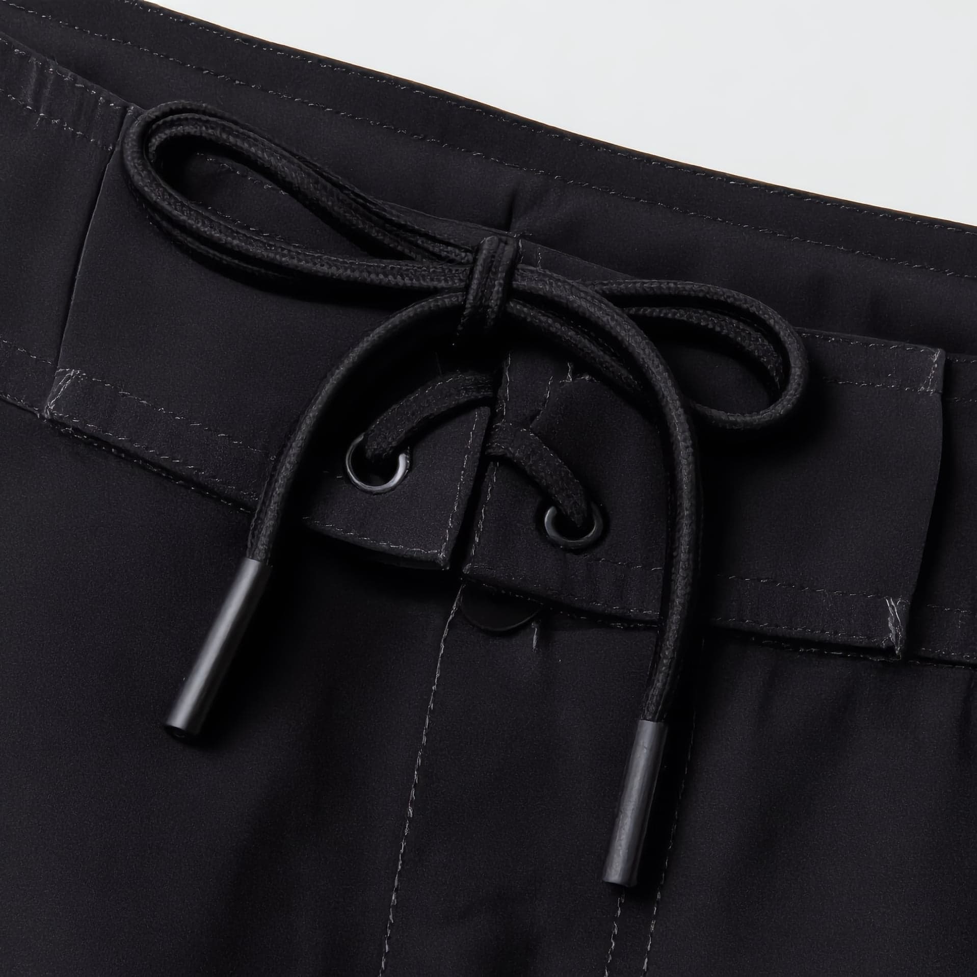 Close view of the waistband: a flat lace tied through two eyelets, tipped with hard aglets, over a fly closure.